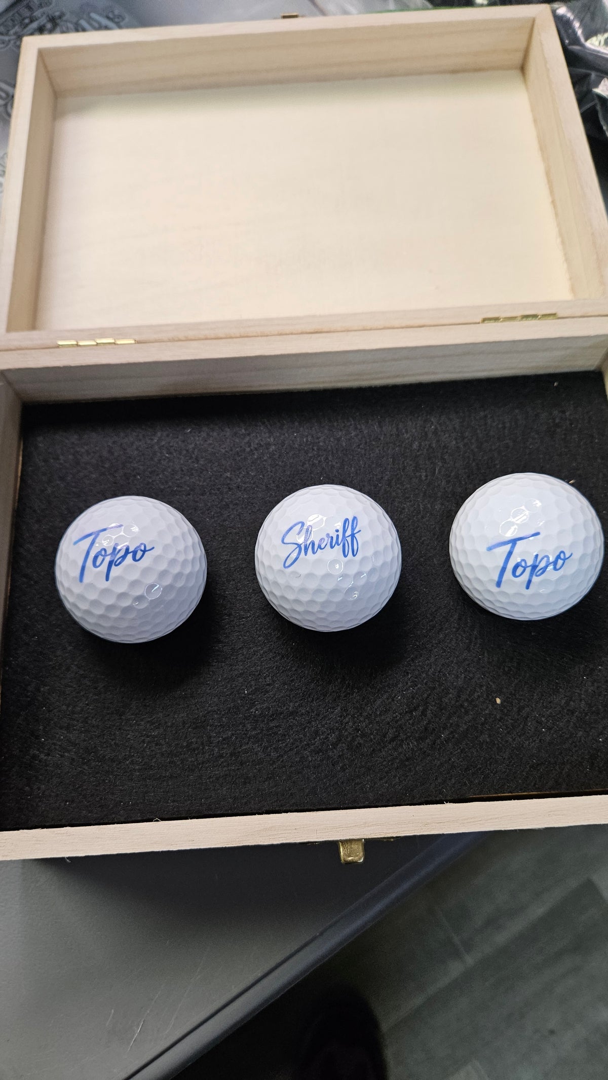 Wooden golf gift box holding three personalized golf balls printed with names in blue script